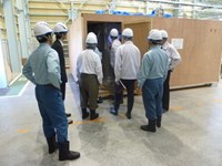 The ITER delegation inspects a wooden crate containing a completed toroidal field conductor unit length ready to be shipped by Nippon Steel Engineering for storage in a nearby warehouse. (Click to view larger version...)