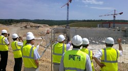 Under the sun of Provence, the delegation looks toward the Tokamak's anti-seismic ''pillows'' and listens to Tim Watson (pointing), director for Buildings & Site Infrastructure, as he relates the latest on ITER construction. (Click to view larger version...)