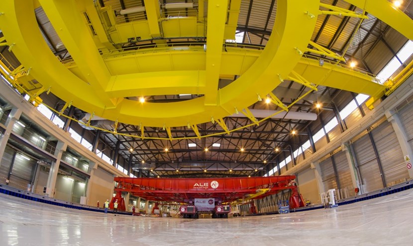 The yellow spreader beam in the foreground, with a lifting capacity of 40 tonnes, will handle the individual ''double pancakes.'' Once the double pancakes are assembled into a coil, they will be manipulated throughout the last stages of fabrication by the red gantry crane. (Click to view larger version...)