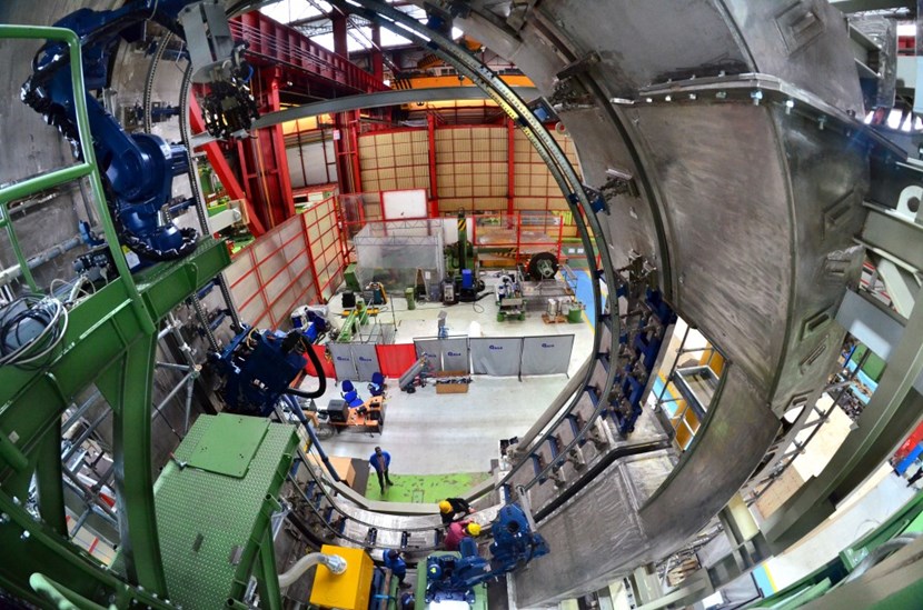 An inside view of the mockup: to the right, a welding robot sits on its support as the weld cap machining tool slowly creeps along the railing, smoothing the weld surface as it moves. A second robot is visible at the bottom of the image (centre), its welding head reaching deep into the gap between the two sectors. (Click to view larger version...)