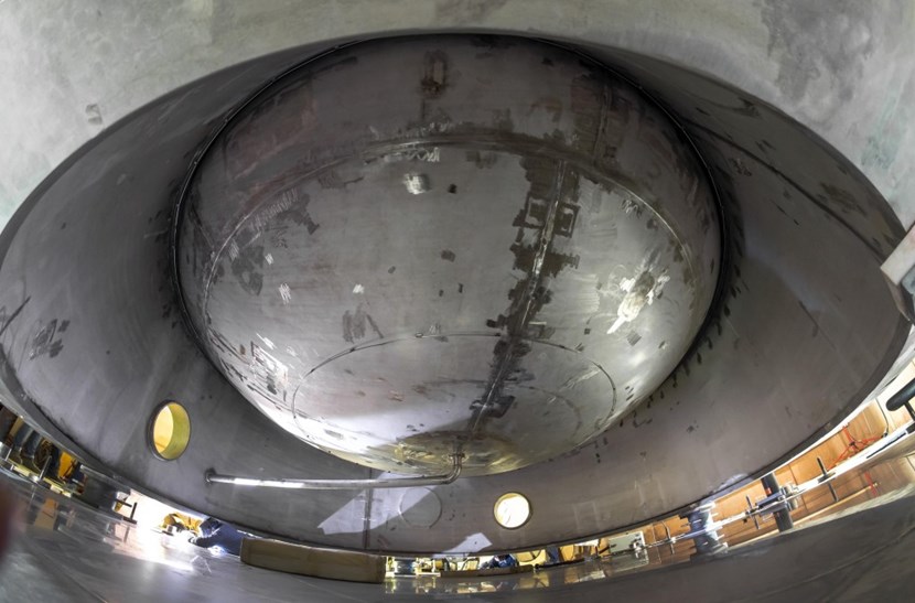 Lying on the floor at the edge of the tank's skirt, a specialist from Italian contractor Cestaro Rossi is welding the final anchorage system (anchor bolts, shear pins and seal lids) to the steel plates deeply embedded in the concrete floor. (Click to view larger version...)