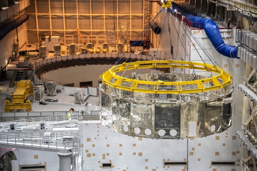 Attached to its ''strong back,'' the 50-tonne lower cryostat thermal shield has reached cruising altitude (23 metres) and speed (2 metres/minute). Its silvery surface reflects the colours, lights and distorted shapes of the environment. (Click to view larger version...)